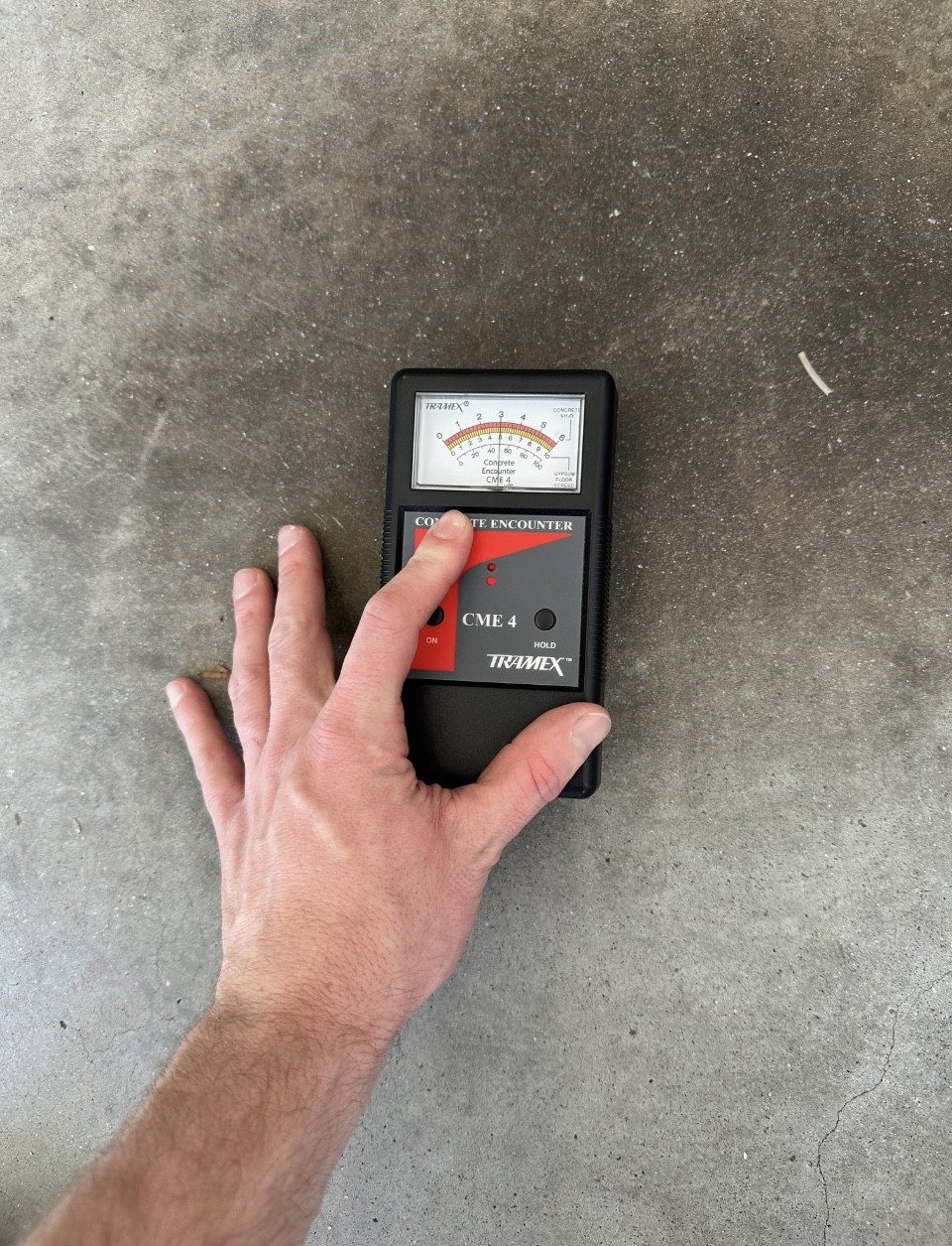 Hand holding a moisture meter on bare concrete